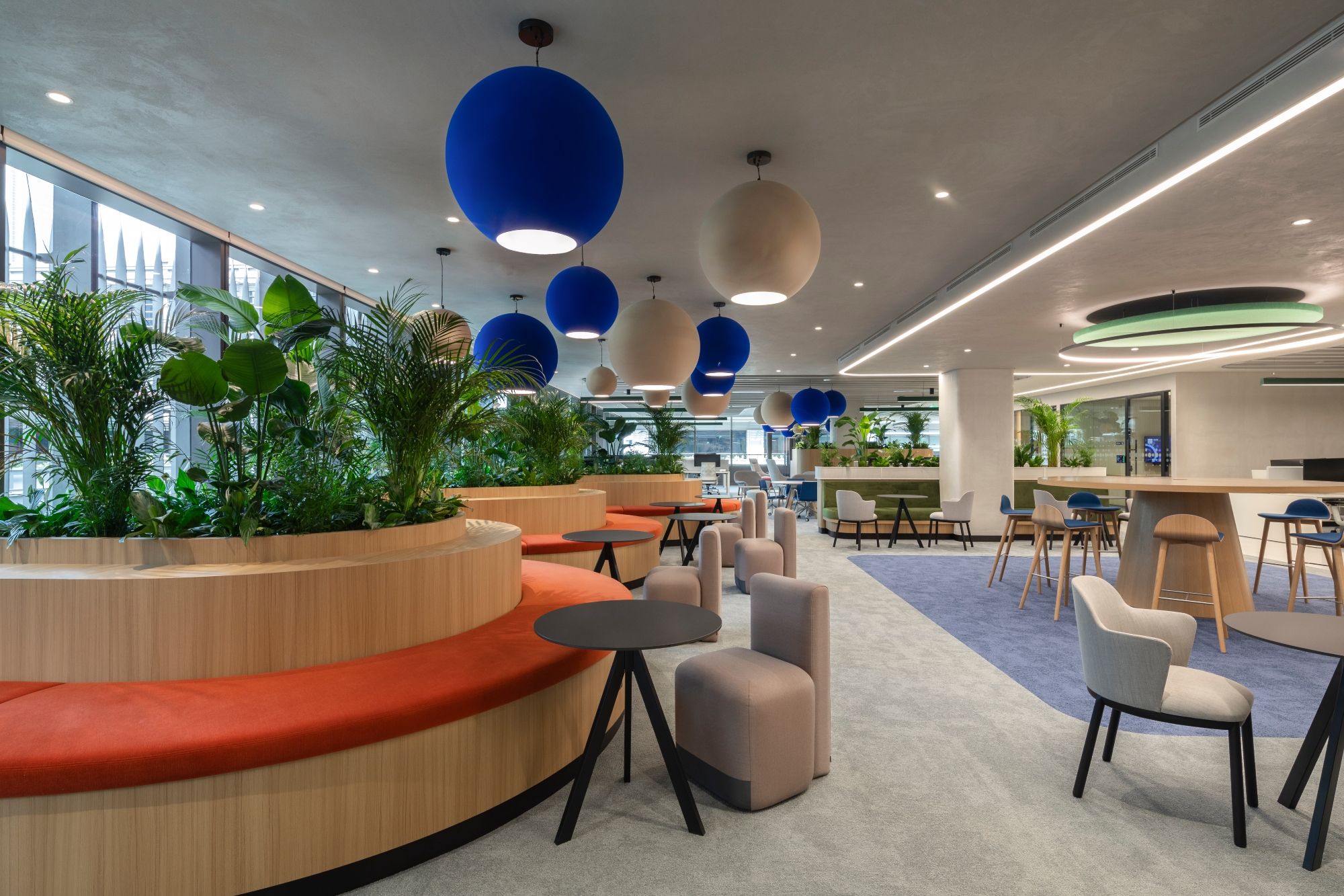 Biophilic open-plan workspace at Informa Dubai designed by dwp, with integrated planting, collaborative seating and bold blue pendant lights.