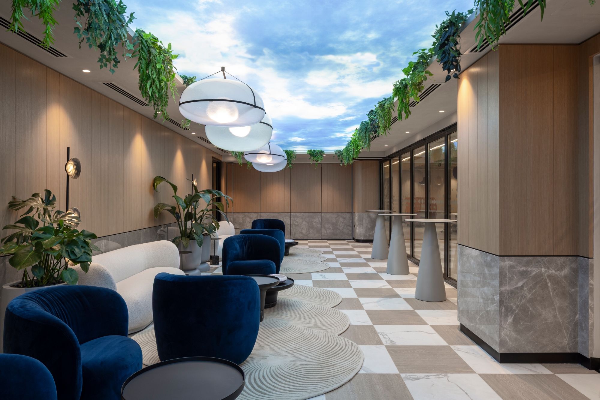Pre-function area outside the Informa Dubai training rooms, with lush planting, timber finishes, marble details and informal lounge seating.