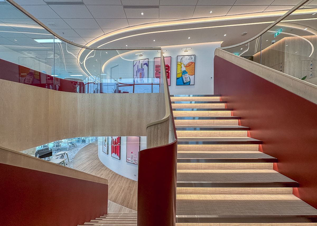 Curved feature staircase connecting three floors of the L’Oréal Bangkok office with red accents and integrated lighting